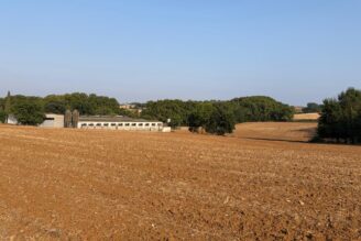 Un camp, amb una granja al fons, al terme de Camós, al Pla de lEstany